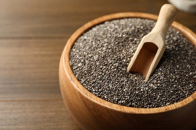 Photo of Wooden bowl with chia seeds and scoop on table, closeup