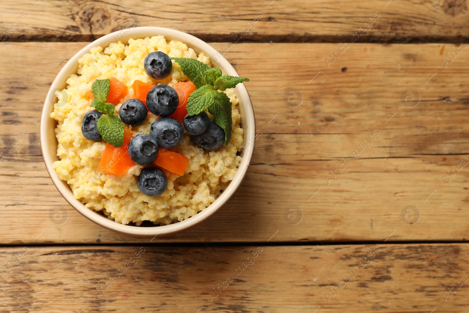 Photo of Tasty millet porridge with blueberries, pumpkin and mint in bowl on wooden table, top view. Space for text