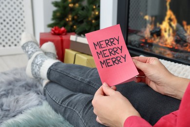 Young woman with greeting card sitting near fireplace indoors, closeup. Space for text