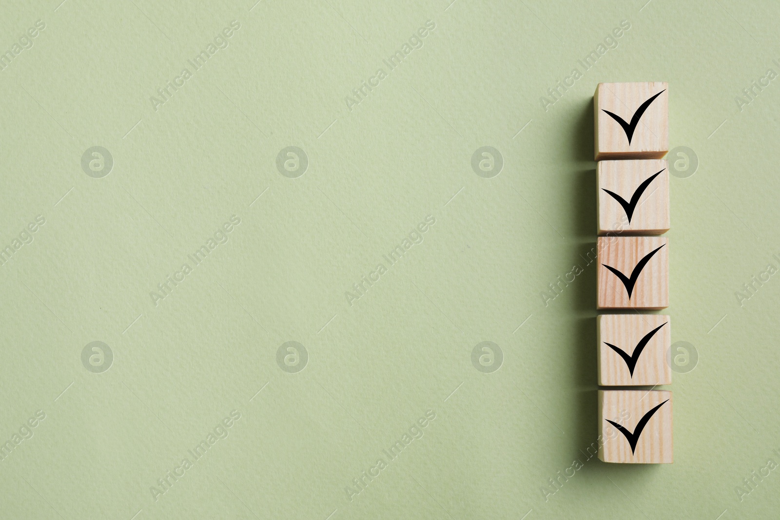 Image of Wooden cubes with check marks on light olive color background, top view. Space for text