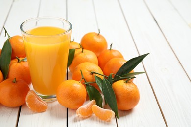 Glass of fresh tangerine juice and fruits on white wooden table