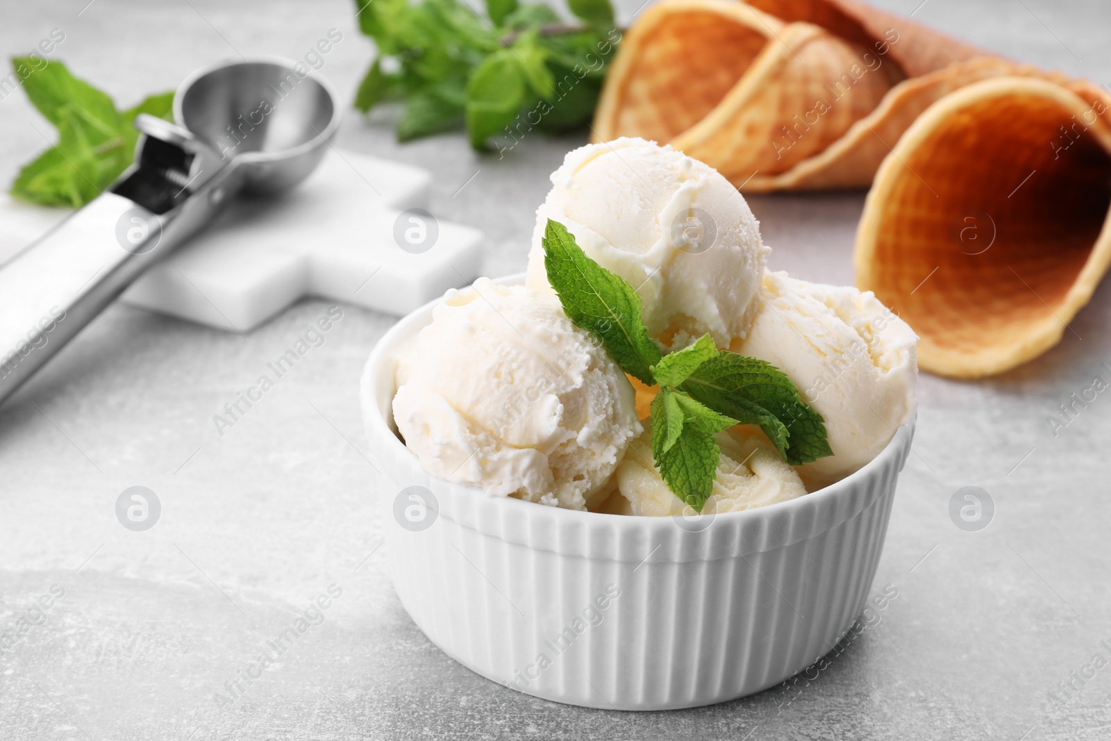 Photo of Delicious vanilla ice cream with mint on light grey table, closeup