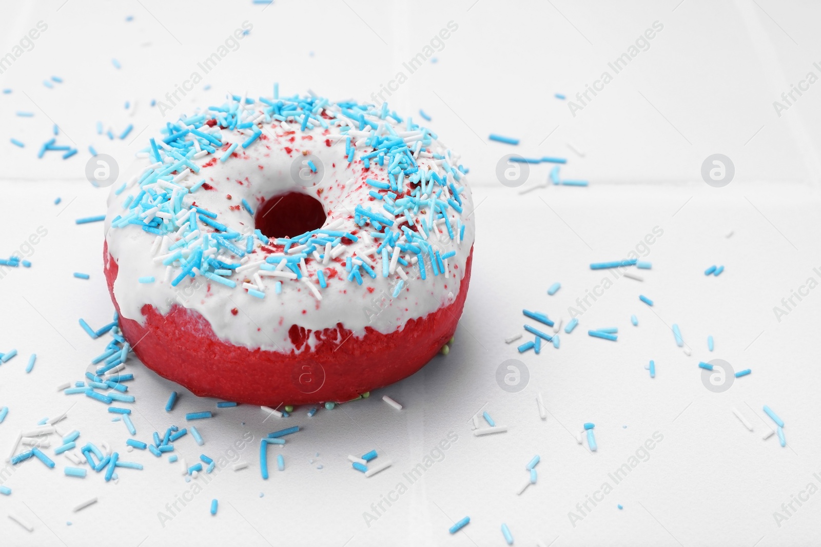 Photo of Glazed donut decorated with sprinkles on white tiled table, closeup. Space for text. Tasty confectionery