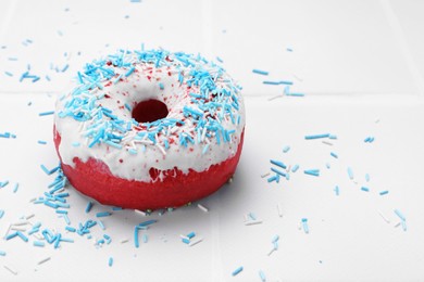 Photo of Glazed donut decorated with sprinkles on white tiled table, closeup. Space for text. Tasty confectionery