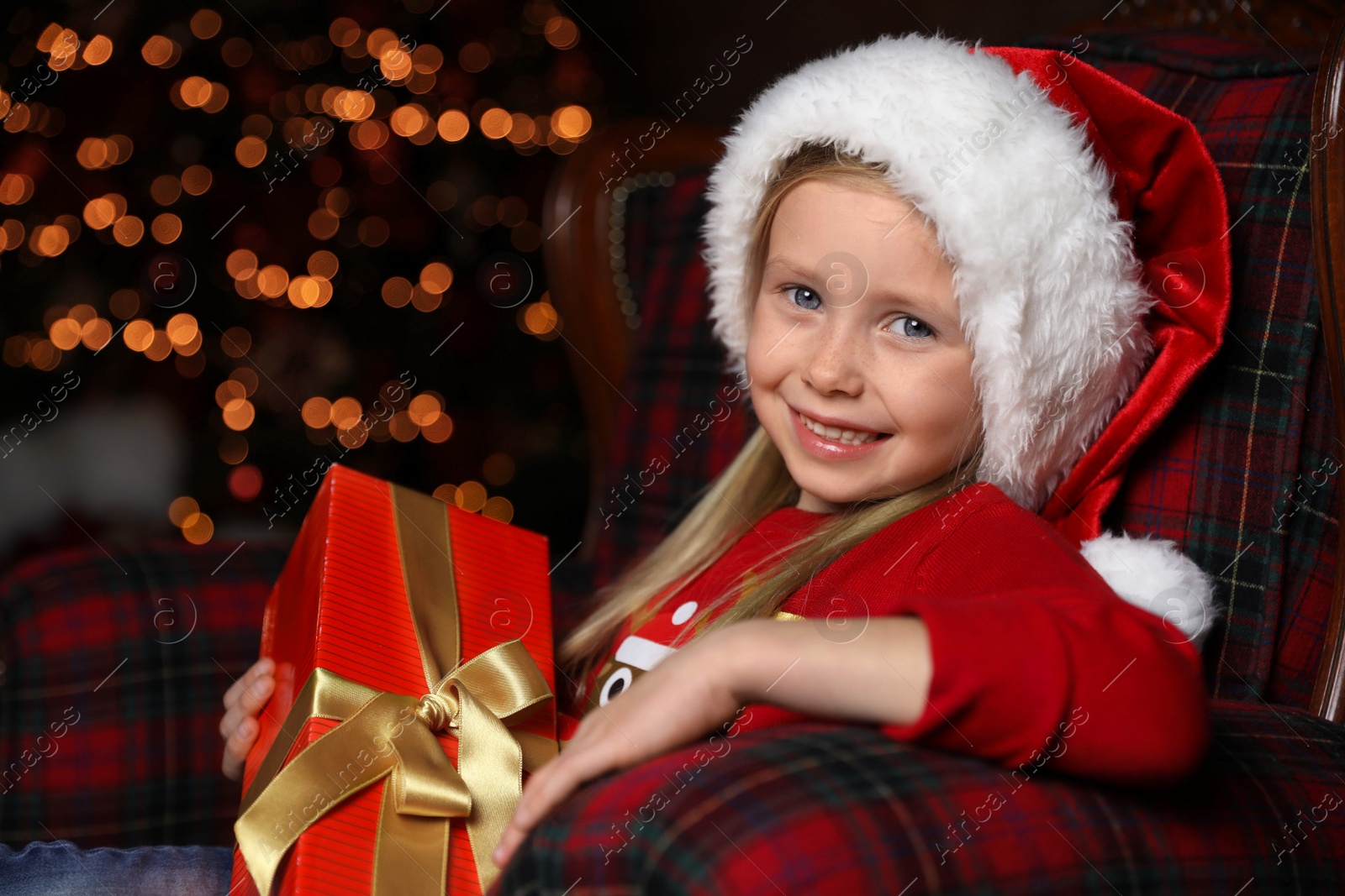 Photo of Cute little child with Christmas gift sitting in armchair at home