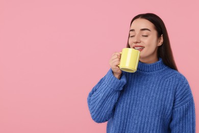 Photo of Happy young woman drinking beverage from yellow ceramic mug on pink background, space for text