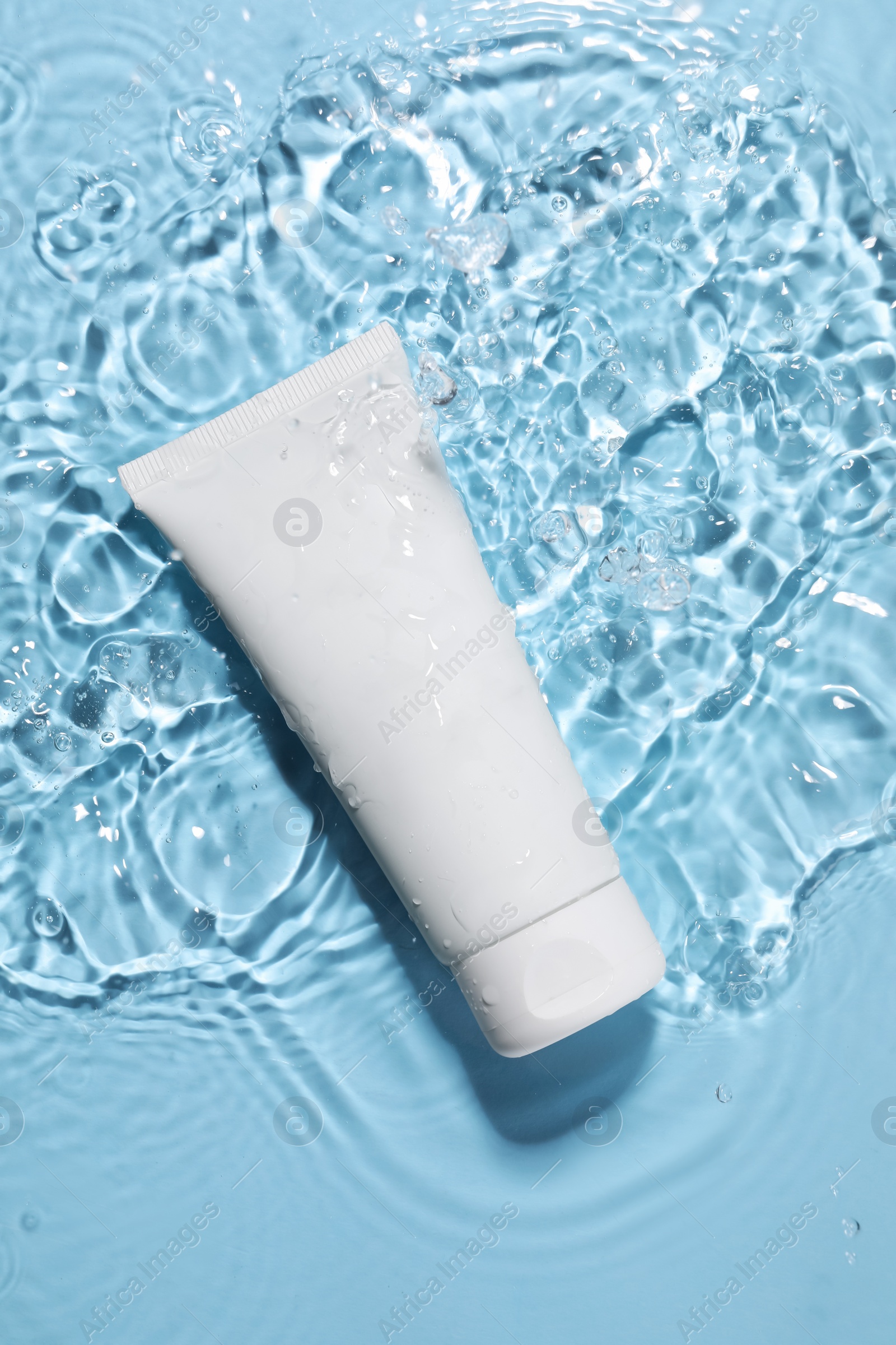 Photo of Tube of face cleansing product in water against light blue background, top view