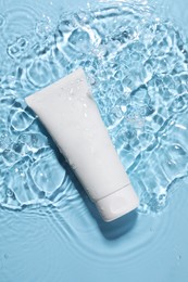 Tube of face cleansing product in water against light blue background, top view