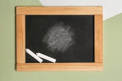 Photo of Small blackboard with chalk hanging on color wall