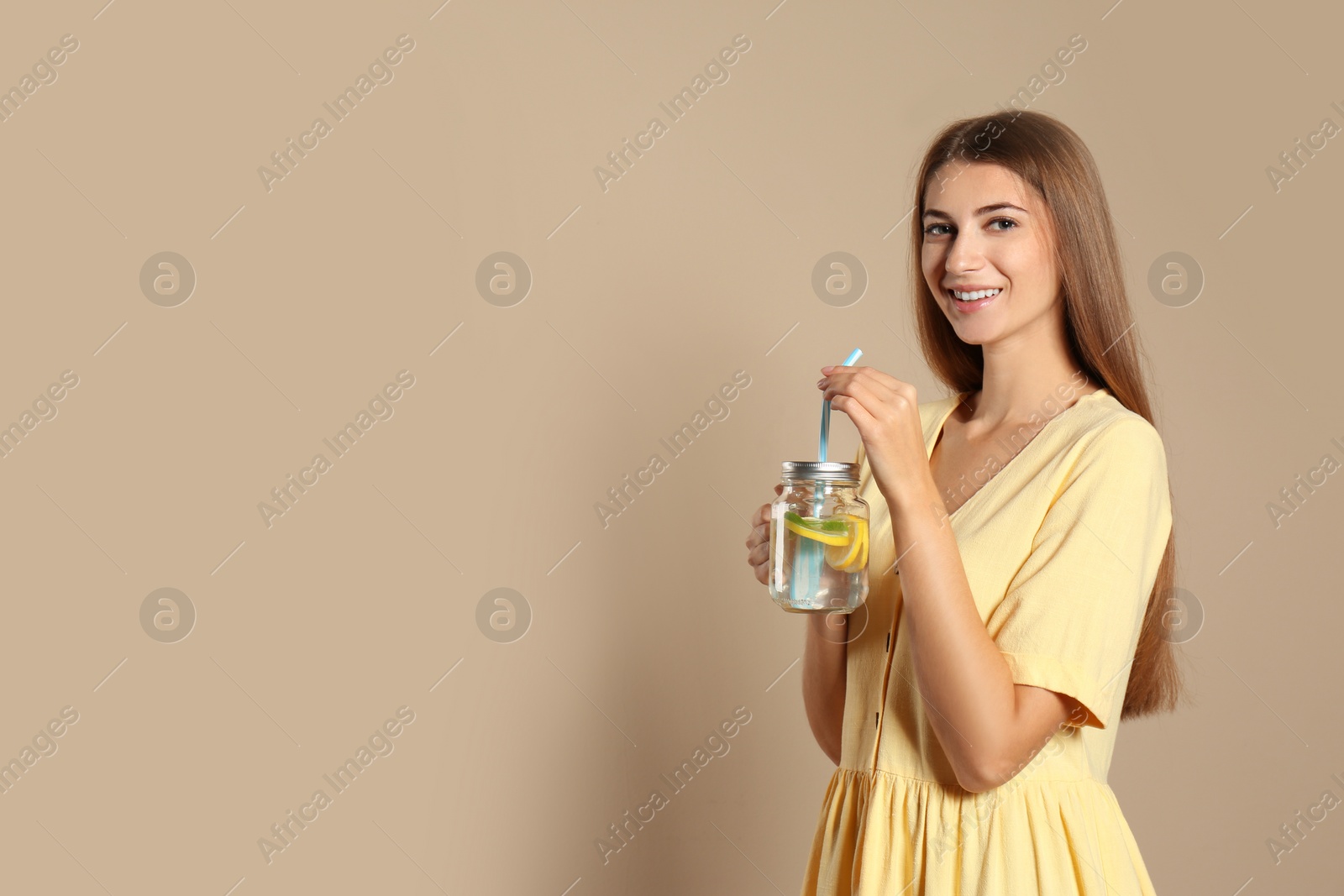 Photo of Young woman with glass of lemon water on beige  background. Space for text