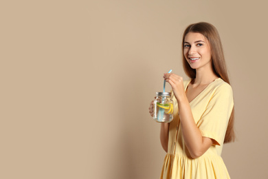 Young woman with glass of lemon water on beige  background. Space for text