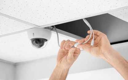 Technician installing CCTV camera on ceiling indoors, closeup