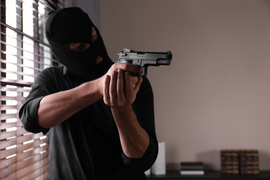 Photo of Man in mask holding gun indoors, focus on hands