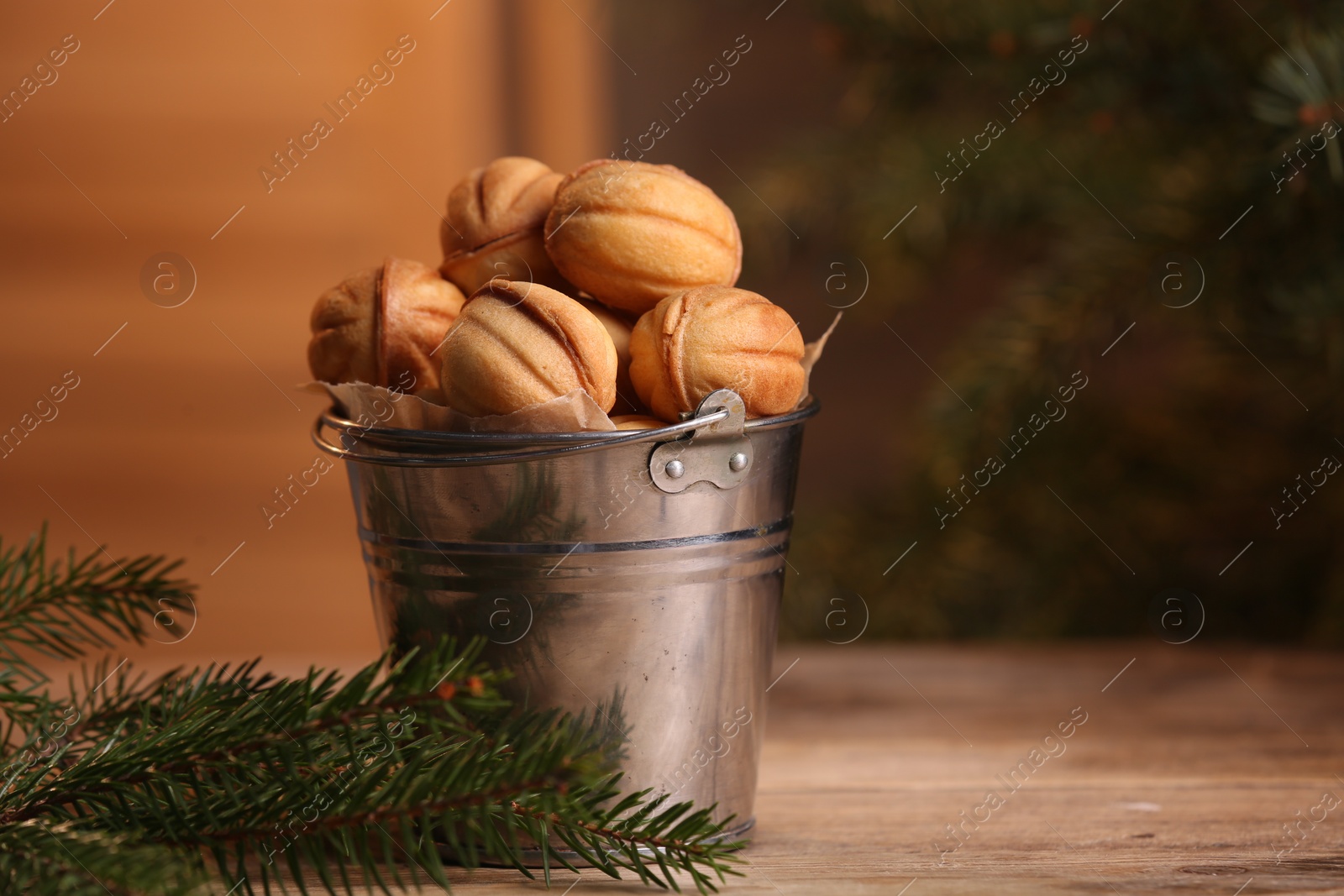 Photo of Metal bucket of delicious nut shaped cookies and fir branches on wooden table, space for text