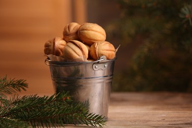 Photo of Metal bucket of delicious nut shaped cookies and fir branches on wooden table, space for text