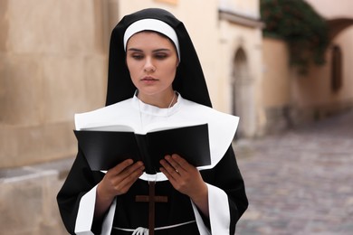Photo of Young nun reading Bible near building outdoors