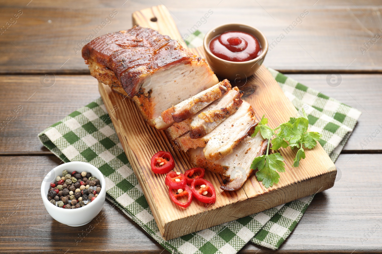 Photo of Pieces of baked pork belly served with sauce, chili pepper and parsley on wooden table