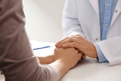 Male doctor comforting woman at table, closeup of hands. Help and support concept