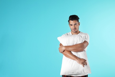 Young man with soft pillow on color background