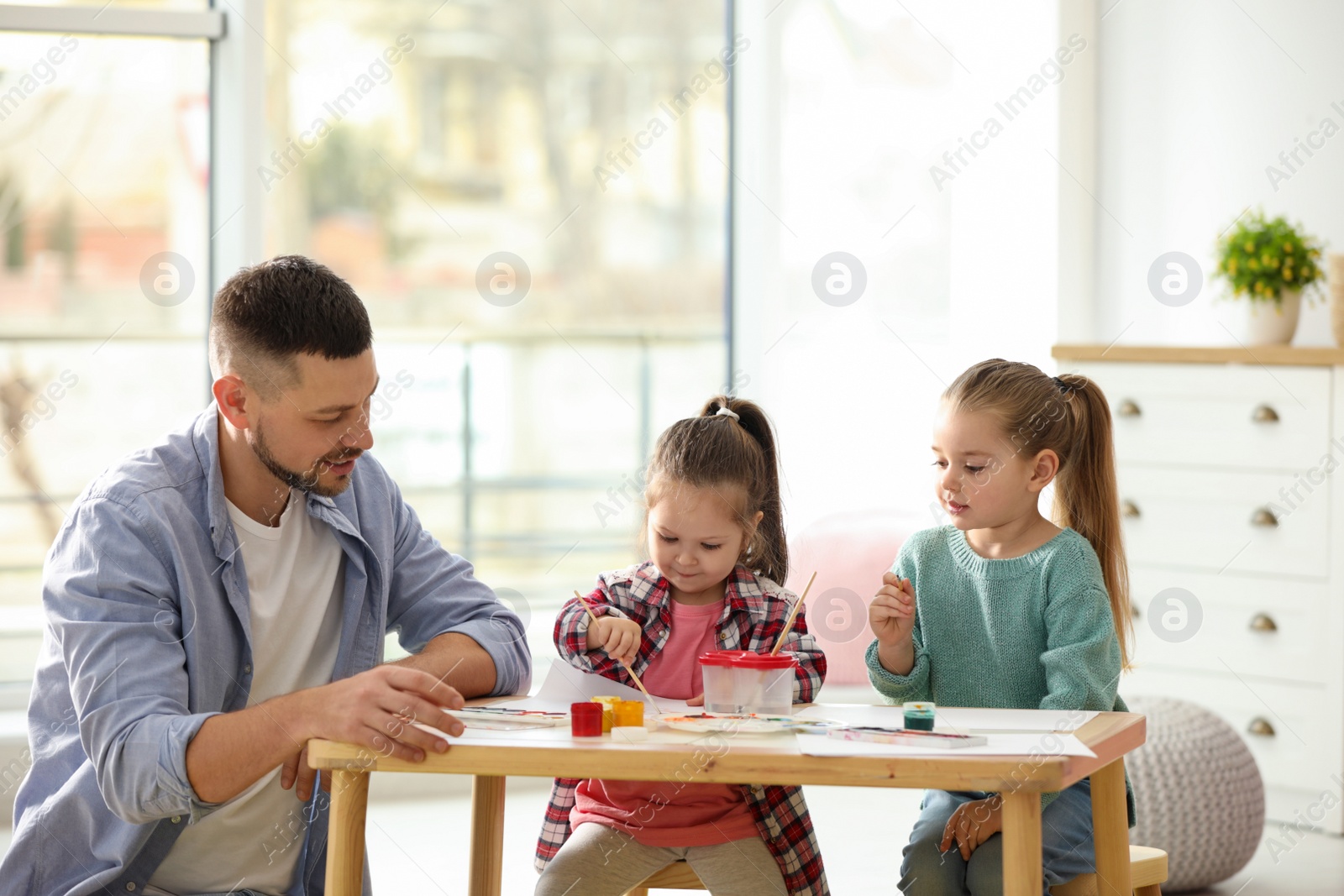 Photo of Father and daughters painting at table indoors. Playing with children