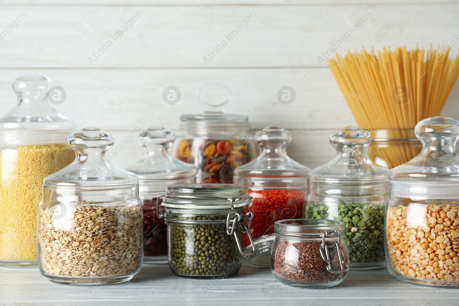 Photo of Glass jars with different types of groats and pasta on white wooden table