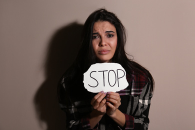 Abused young woman with sign STOP near beige wall. Domestic violence concept
