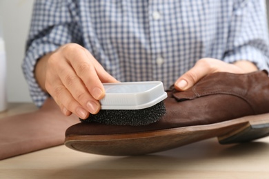 Woman taking care of stylish shoe at wooden table, closeup