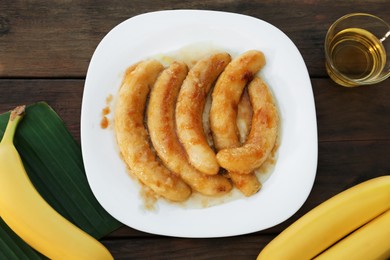 Photo of Delicious fried bananas and oil on wooden table, flat lay