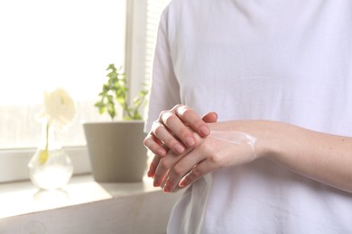 Photo of Woman applying hand cream at home, closeup