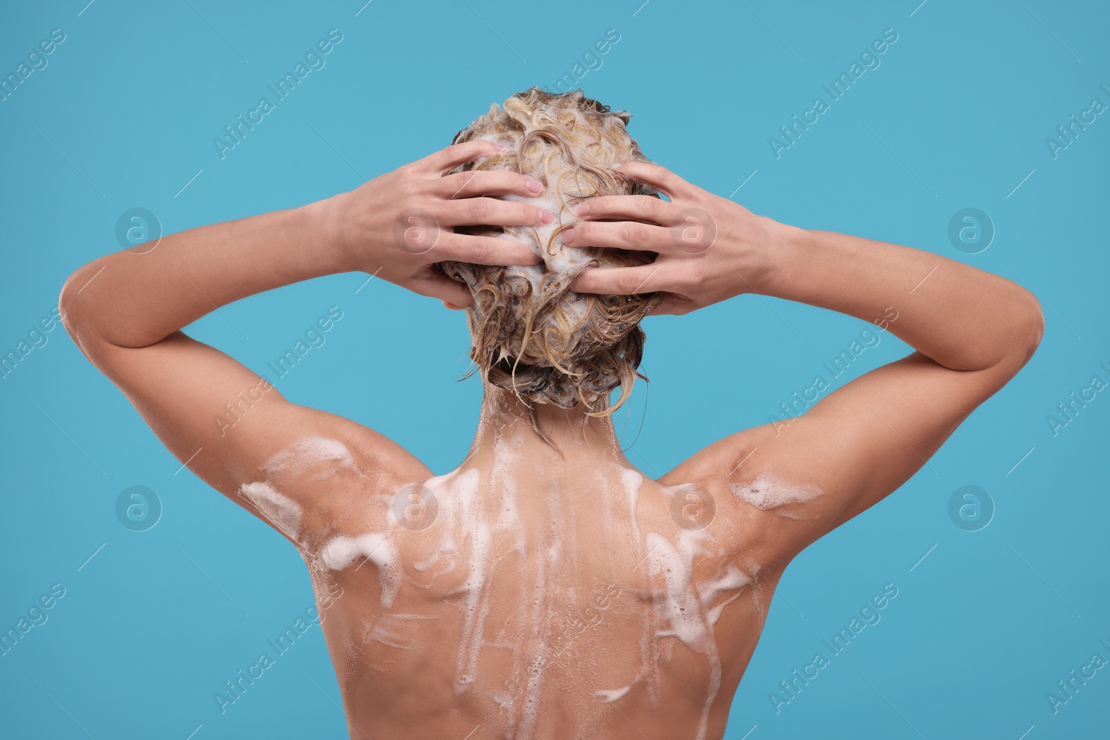 Photo of Woman washing hair on light blue background, back view