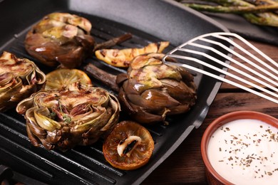 Tasty grilled artichokes with sauce on wooden table, closeup