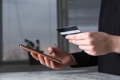 Photo of Online payment. Woman with smartphone and credit card at white marble table indoors, closeup