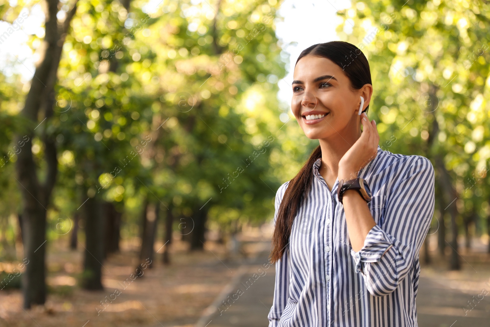 Photo of Young woman with wireless earphones in park