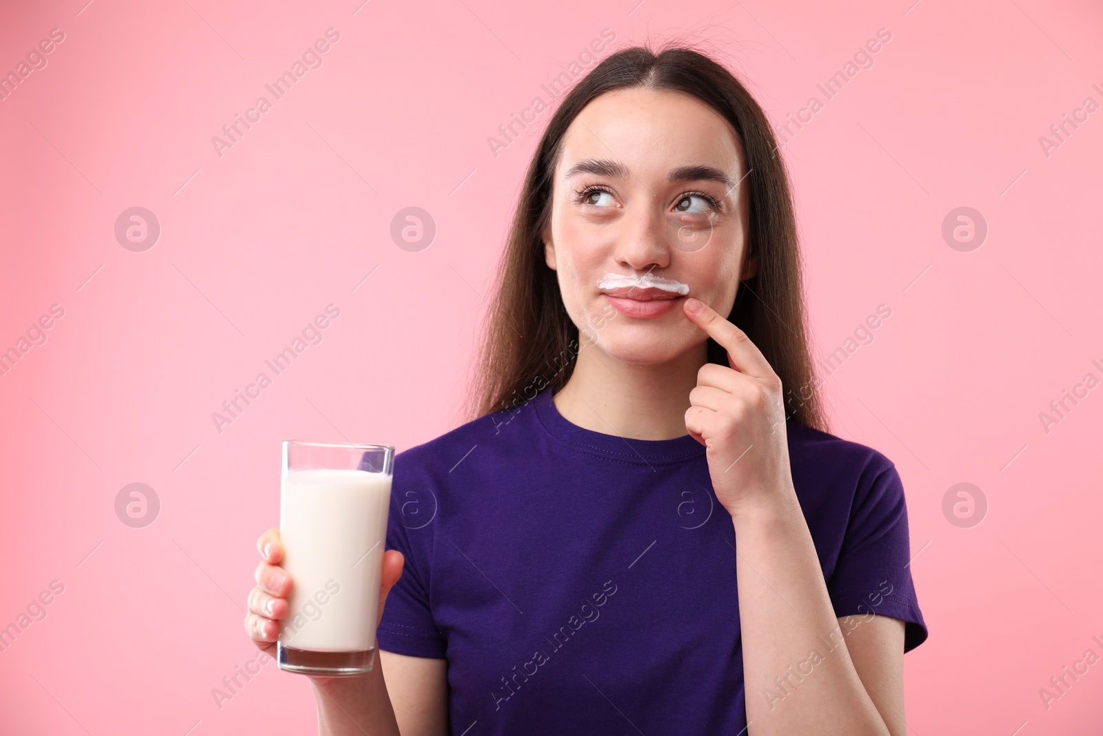 Photo of Cute woman with milk mustache holding glass of tasty dairy drink on pink background