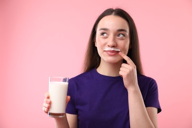 Photo of Cute woman with milk mustache holding glass of tasty dairy drink on pink background