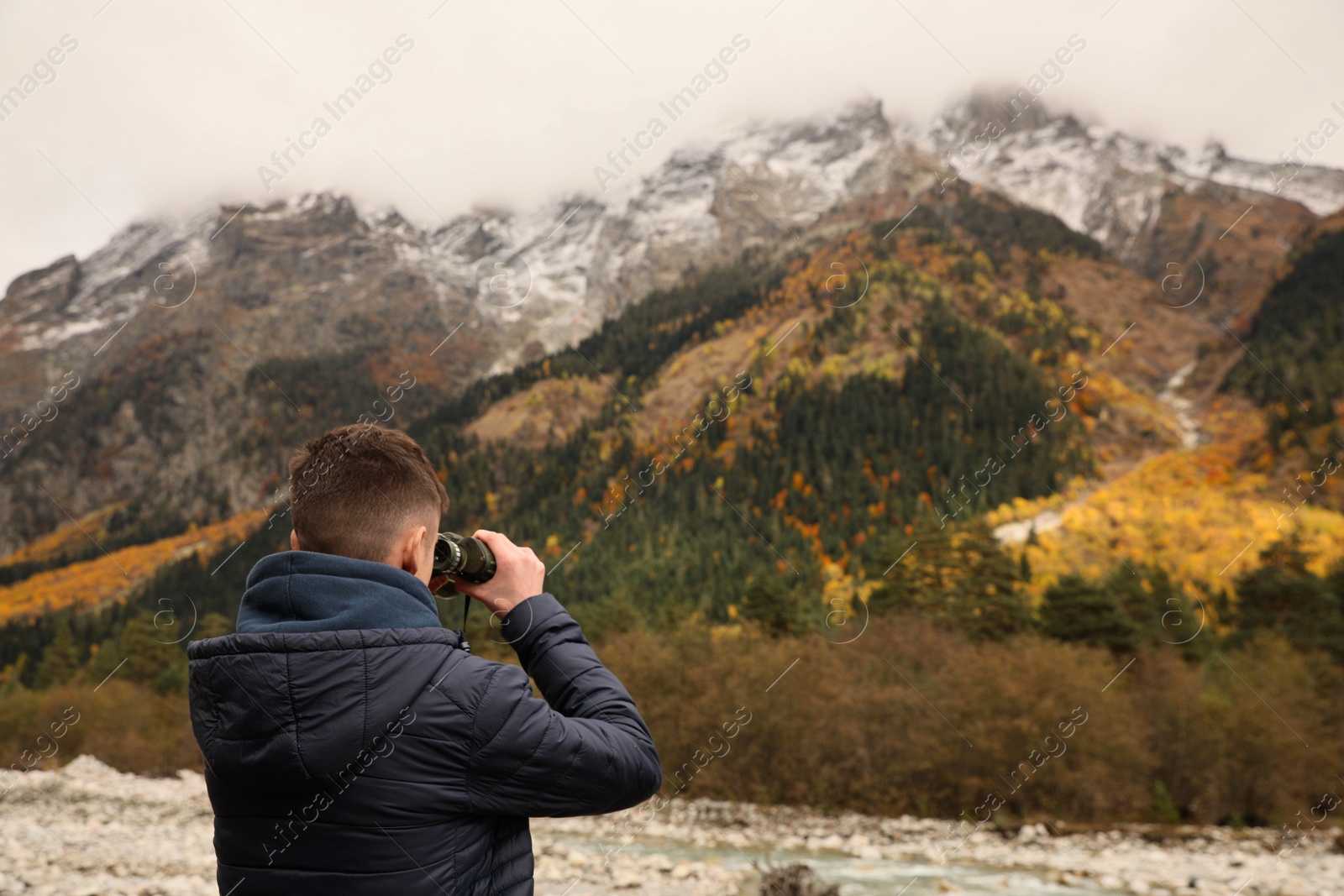 Photo of Boy looking through binoculars in beautiful mountains, back view. Space for text