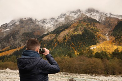 Boy looking through binoculars in beautiful mountains, back view. Space for text