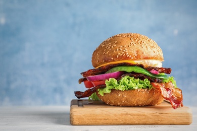 Photo of Fresh juicy bacon burger on white wooden table against blue background. Space for text