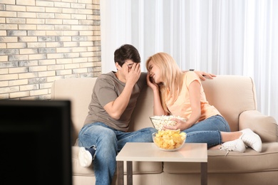 Photo of Young couple with snacks watching TV on sofa at home