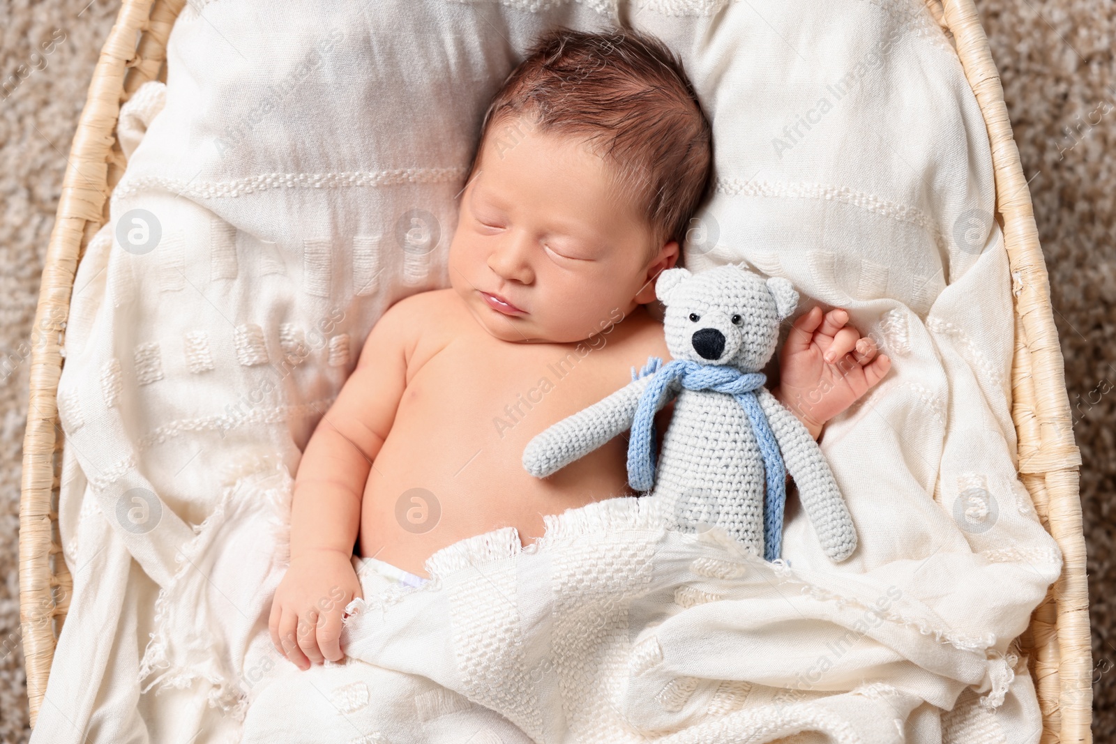 Photo of Cute newborn baby sleeping with toy bear on white blanket in wicker crib, top view