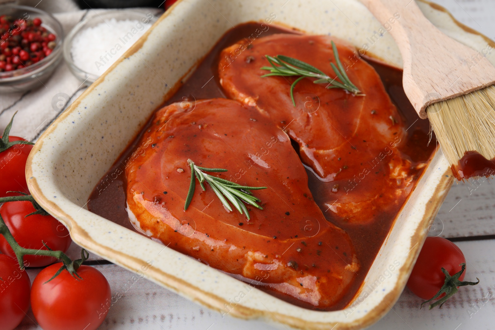 Photo of Raw marinated meat, rosemary and basting brush on white wooden table, closeup