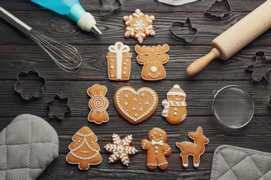 Christmas tree shape made of delicious gingerbread cookies surrounded by kitchen utensils on black wooden table, flat lay