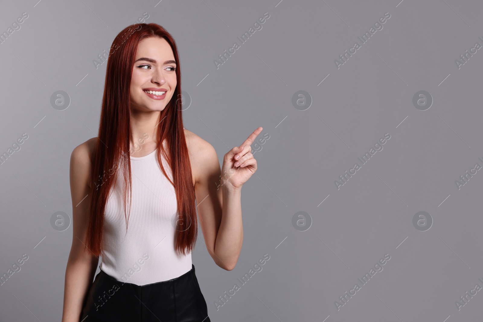 Photo of Happy woman with red dyed hair pointing somewhere on light gray background, space for text