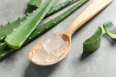 Photo of Spoon with peeled aloe vera and green leaves on gray background