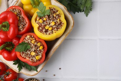 Photo of Quinoa stuffed bell peppers in baking dish, tomatoes and parsley on white tiled table, flat lay. Space for text