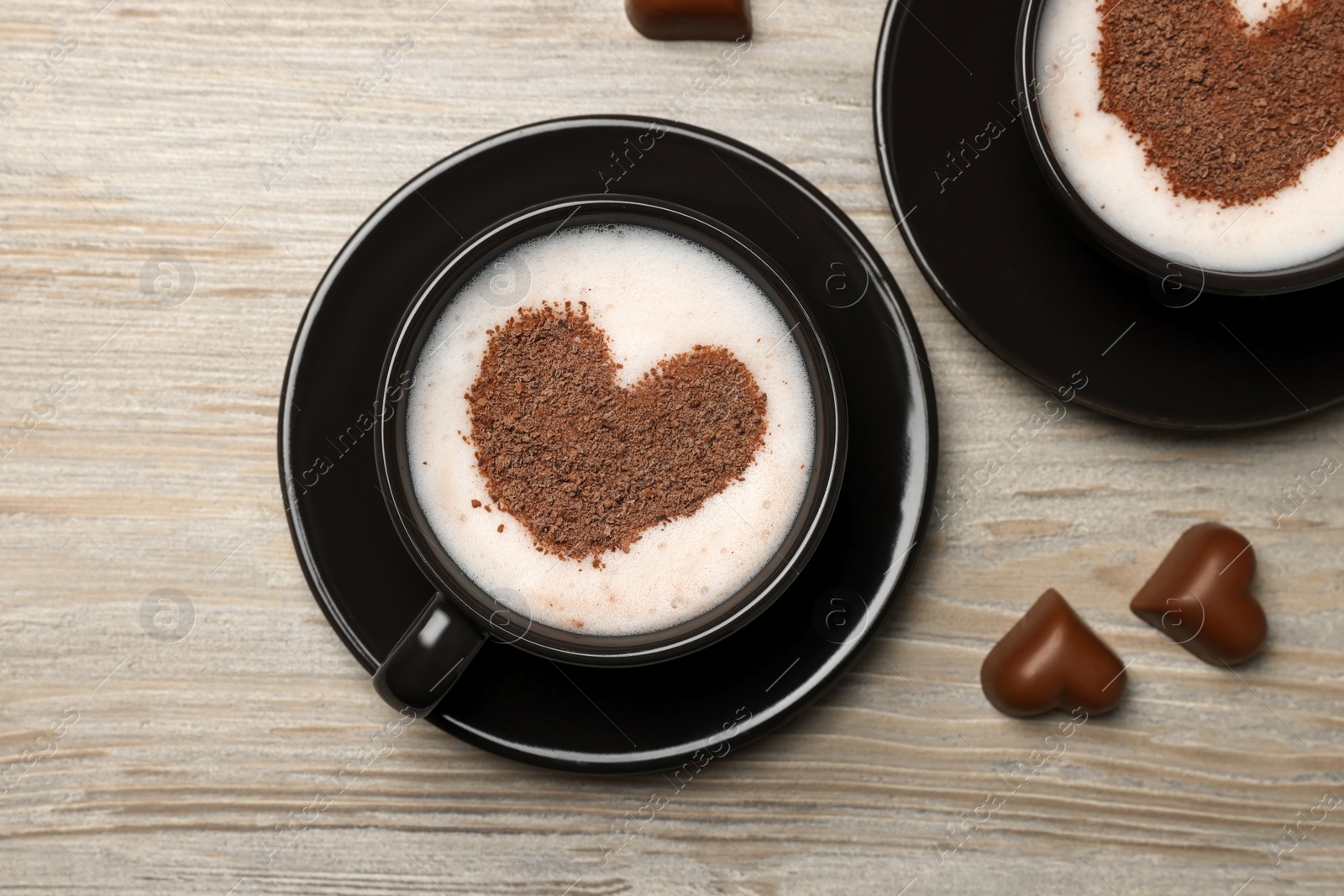 Photo of Cups of aromatic coffee with heart shaped decoration and chocolate candies on wooden table, flat lay