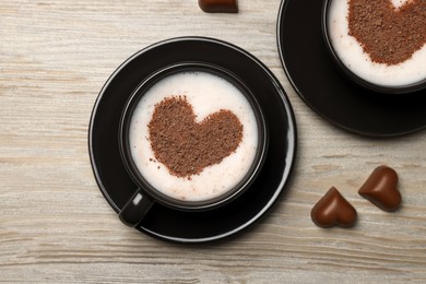 Photo of Cups of aromatic coffee with heart shaped decoration and chocolate candies on wooden table, flat lay
