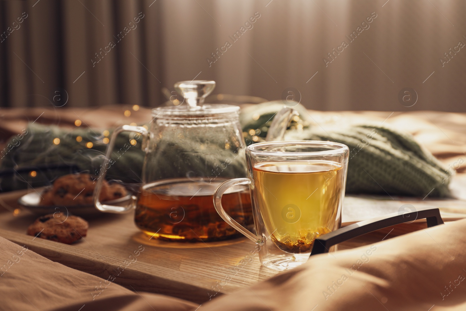 Photo of Wooden tray with freshly brewed tea and cookies on bed in room. Cozy home atmosphere