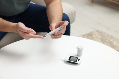 Photo of Diabetes test. Man checking blood sugar level with lancet pen at white table, closeup