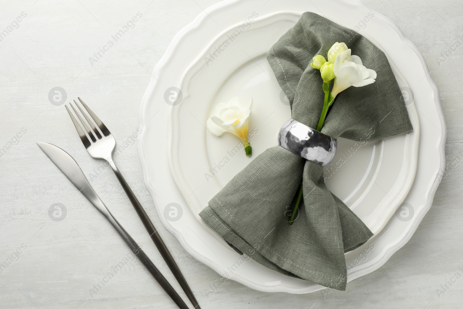Photo of Stylish setting with cutlery, napkin, flowers and plates on light textured table, flat lay